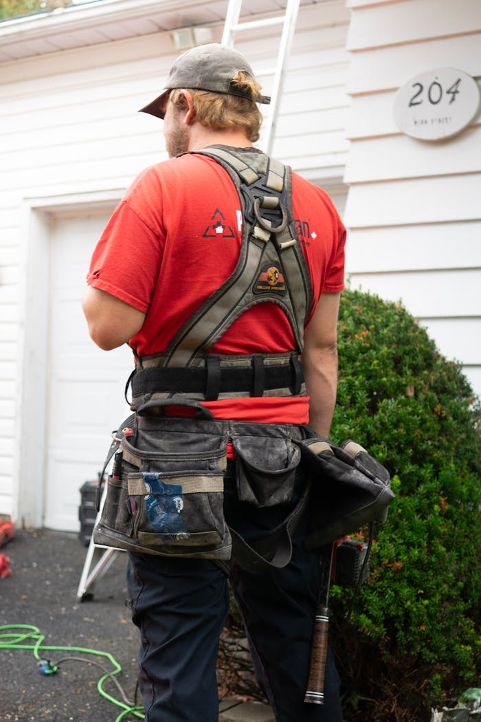 Back view of construction worker in red shirt and safety harness next to a house.