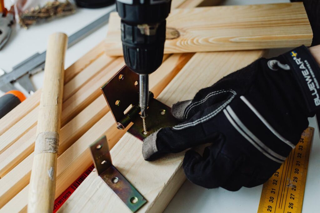 Detailed view of a woodworking project with a power drill, bracket, and safety gloves.